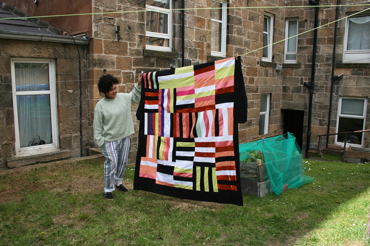 Figure stands next to patterned blanket on a washing line in a garden