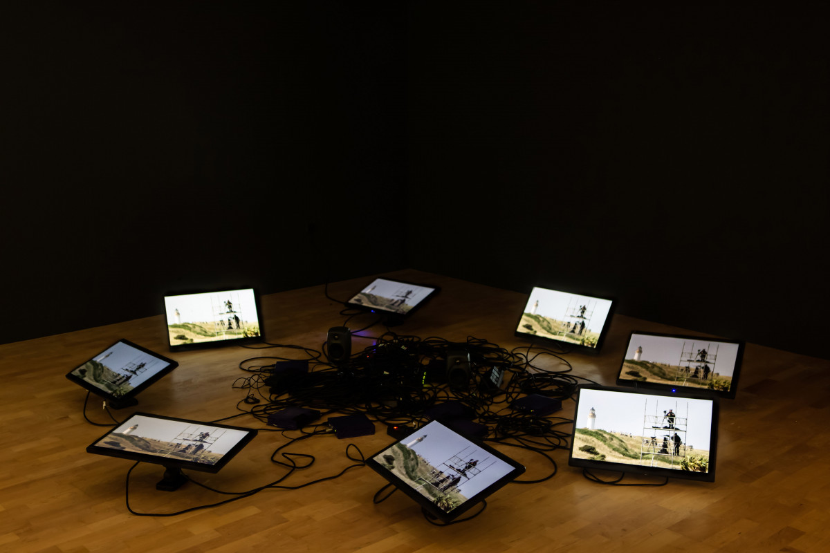 8 tv monitors in a circle on the ground - surrounding a tangle of black wires 