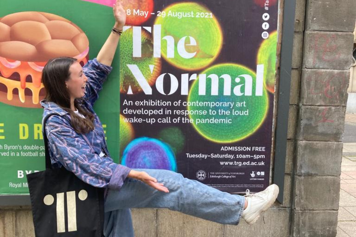 Person wearing black gold bag with arm and leg spread out in front of The Normal poster