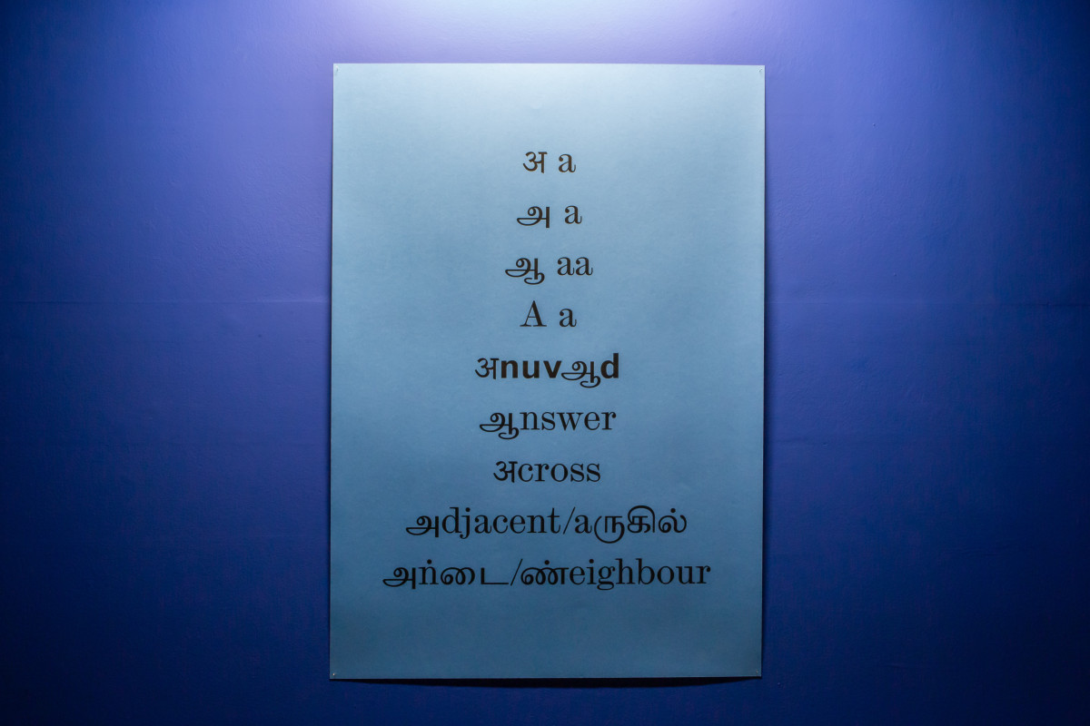 Light blue poster with English and Tamil characters on dark blue wall