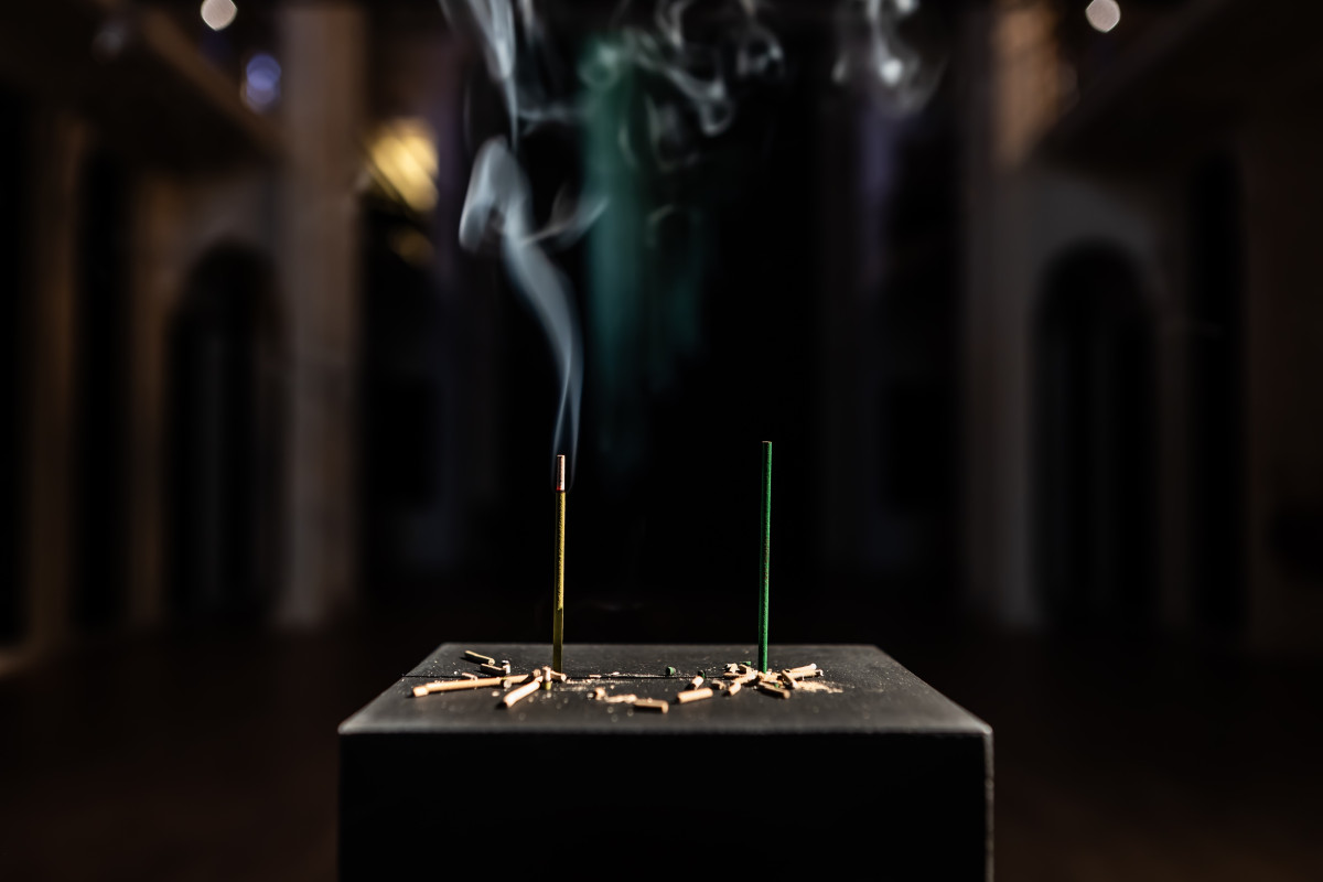 Two green incense sticks on a black platform, with the light green stick on the left burning with smoke.