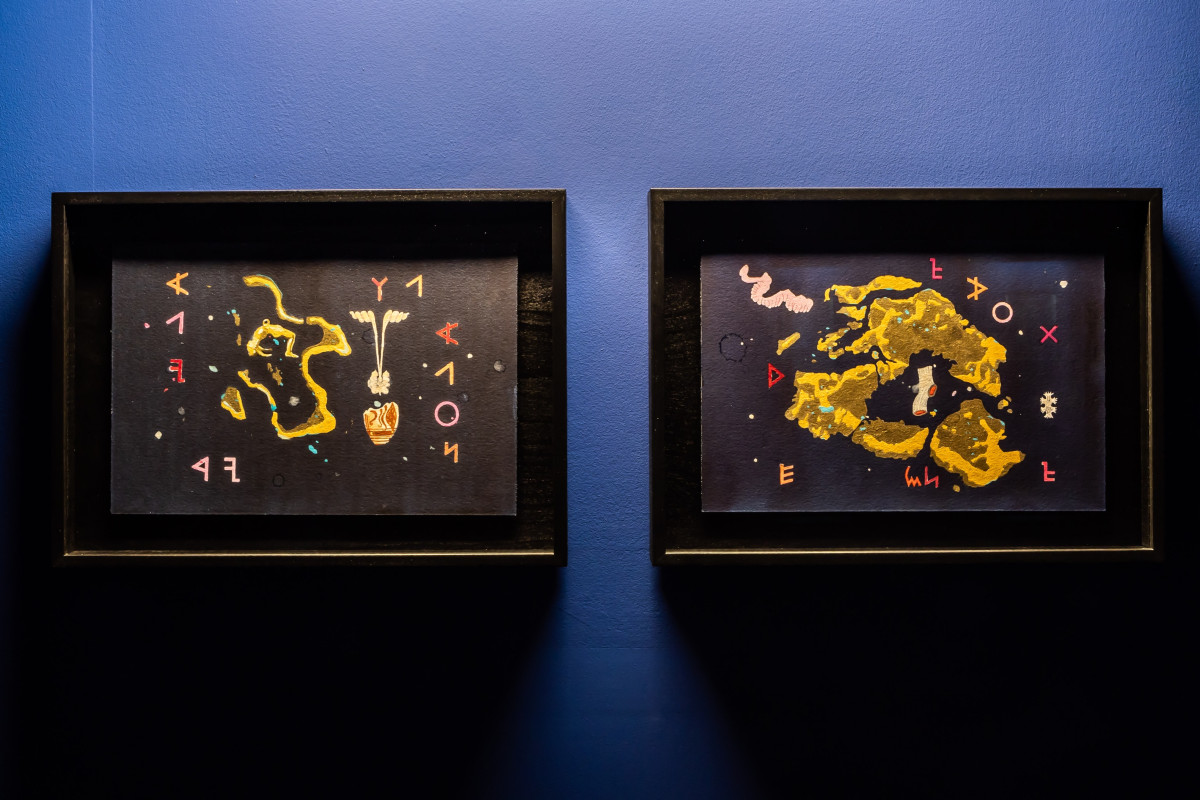 Two framed abstract paintings with yellow, pink and white shapes against a dark blue background.