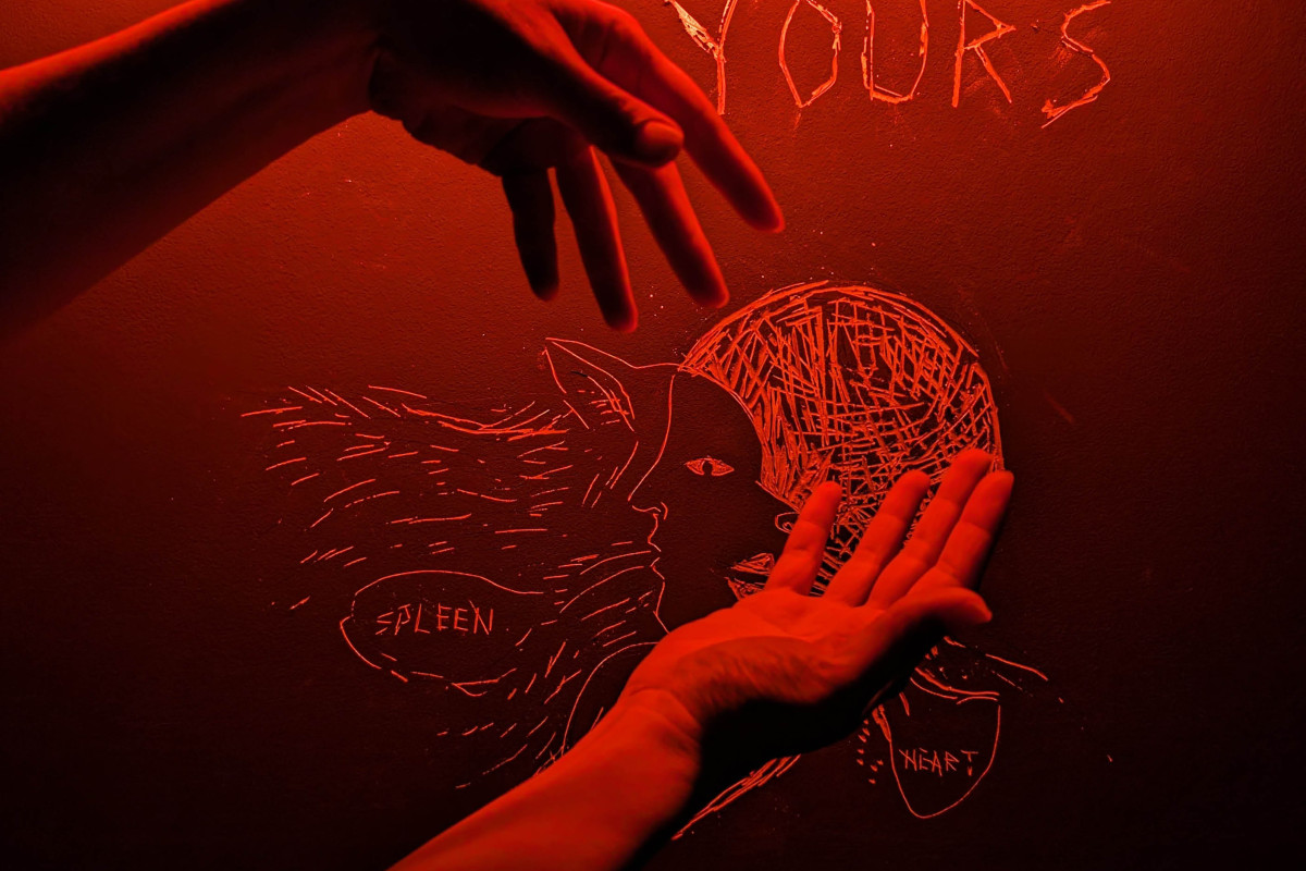 Two hands lifted into the air against a drawing on a wall