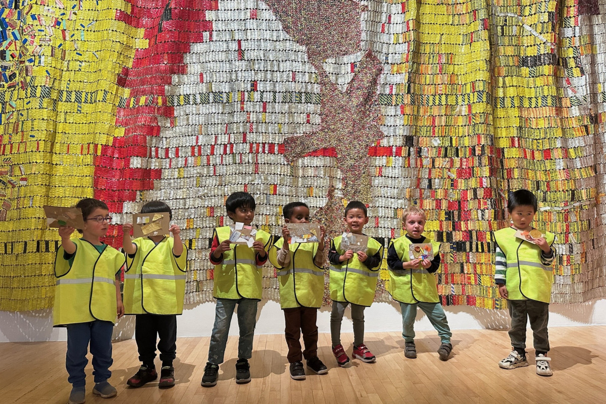 Nursery children in high-vis coats standing in front of El Anatsui artwork