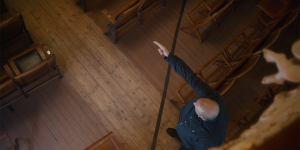 Aerial view of man making gun gesture with hand over a black line in a theatre space with wooden floor planks.