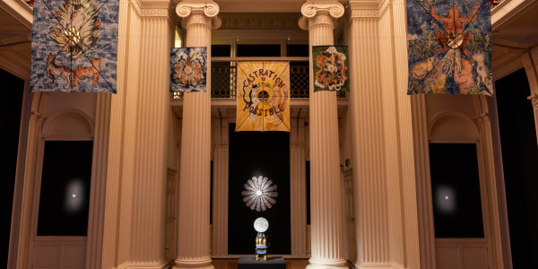 Five kites suspended from a gallery ceiling above a sculpture.