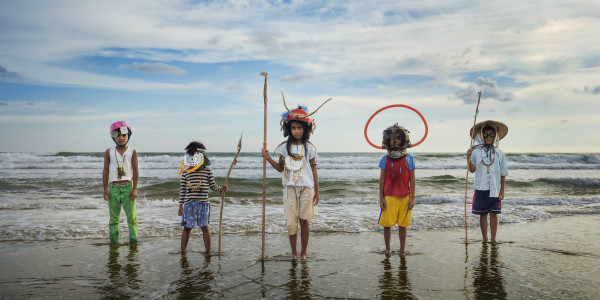Five children in costume standing on a beach with the waves behind them approaching the shore