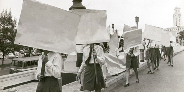 Black white archival photograph of young women carrying protest placards that have been erased